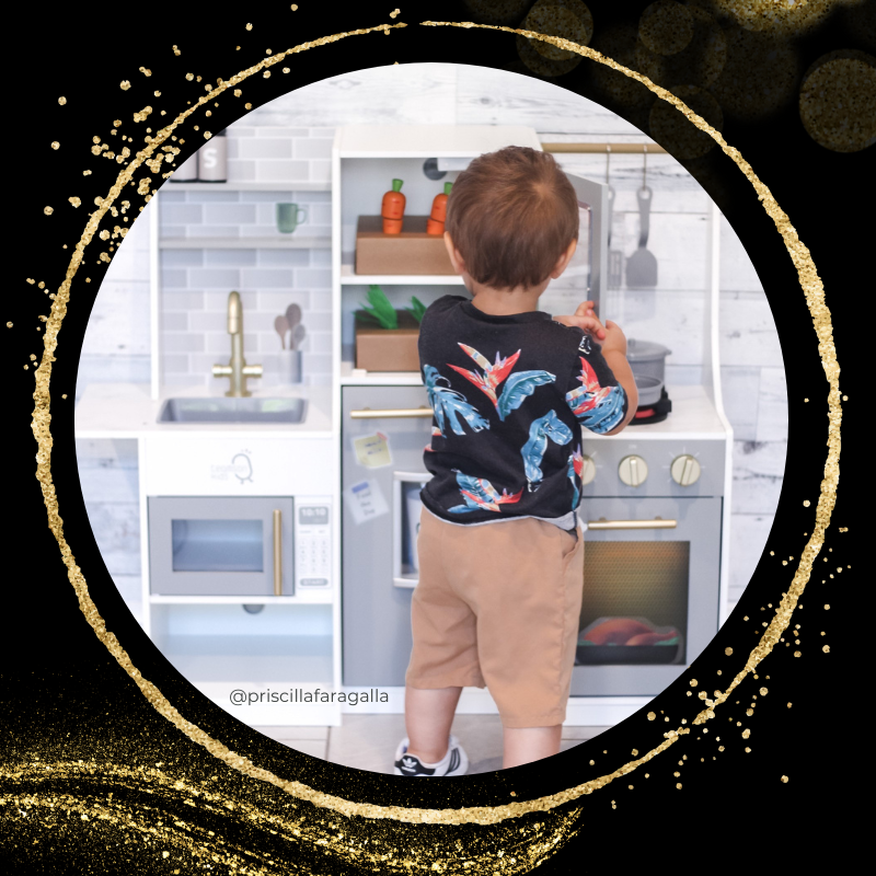 A little boy dressed in blue and khaki playing with a play kitchen