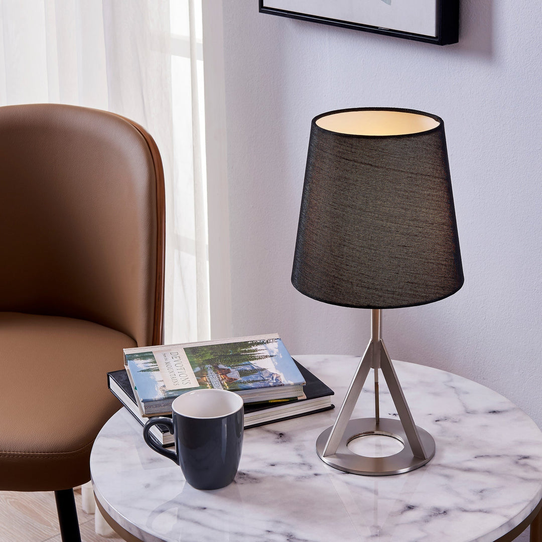 A table lamp with a black shade sits on a faux marble table top next to a blue mug and books