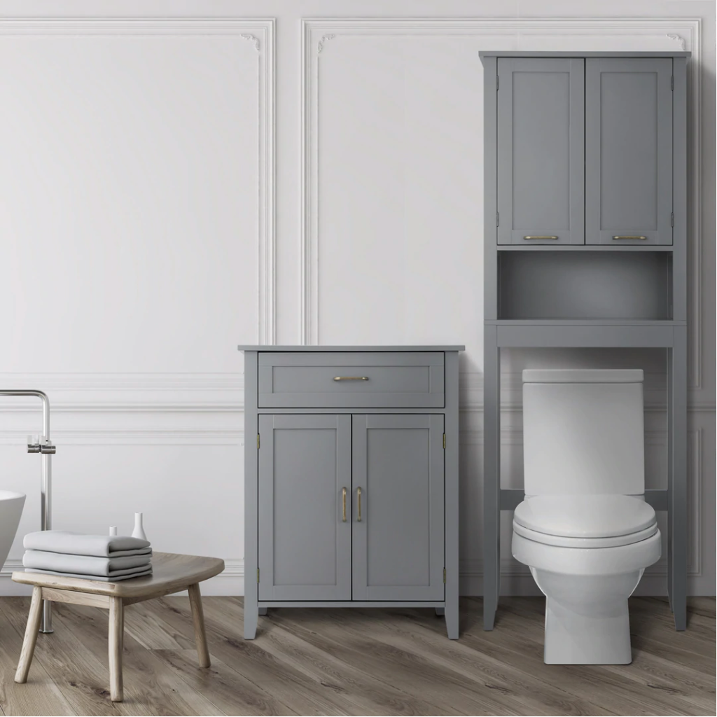 A gray floor cabinet with double doors and a top drawer is placed next to a gray over-the-toilet cabinet with double doors and an open shelf.