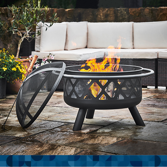 A cast-iron looking wood burning fire pit with a spark screen and poker on a patio.