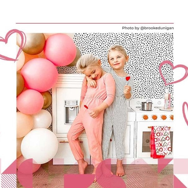 Two girls in pajamas stand in front of their white Teamson kitchen play set.