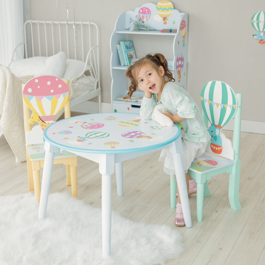 A young girl sits at a child-sized table with hot air balloon themed chairs.