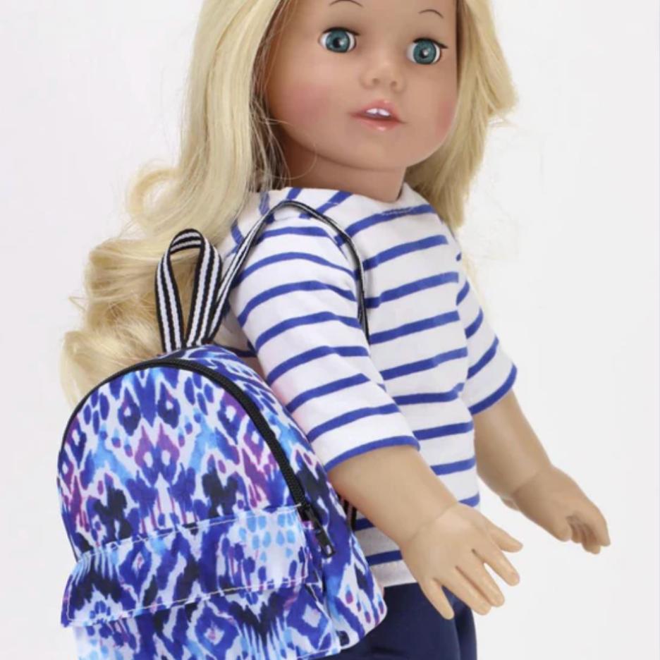 A blonde doll with blue eyes in a blue and white striped shirt has a blue and purple print backpack hanging on her shoulder
