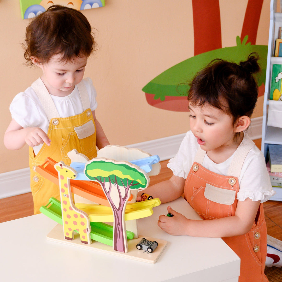 Two young kids playing with a teamson kids toys that features colorful slides and a giraffe.