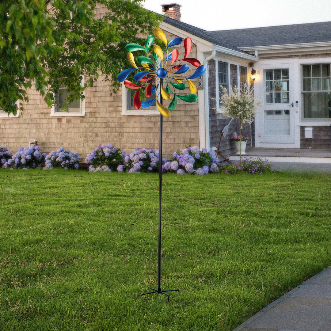 A Metallic Kinetic Windmill Spinner in a front yard with a suburban house and hydrangea bushes in the background.