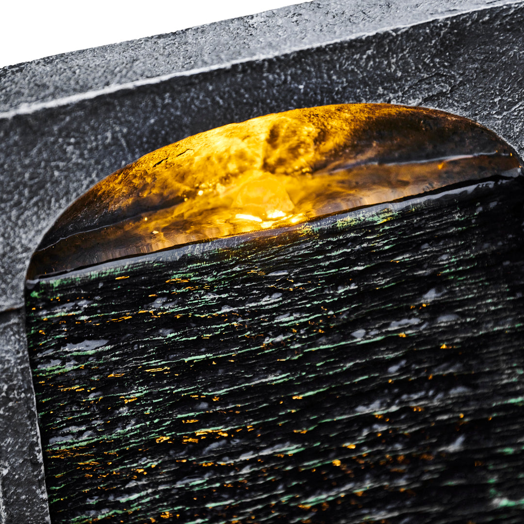 A close-up of the top of a waterfall water fountain with a light