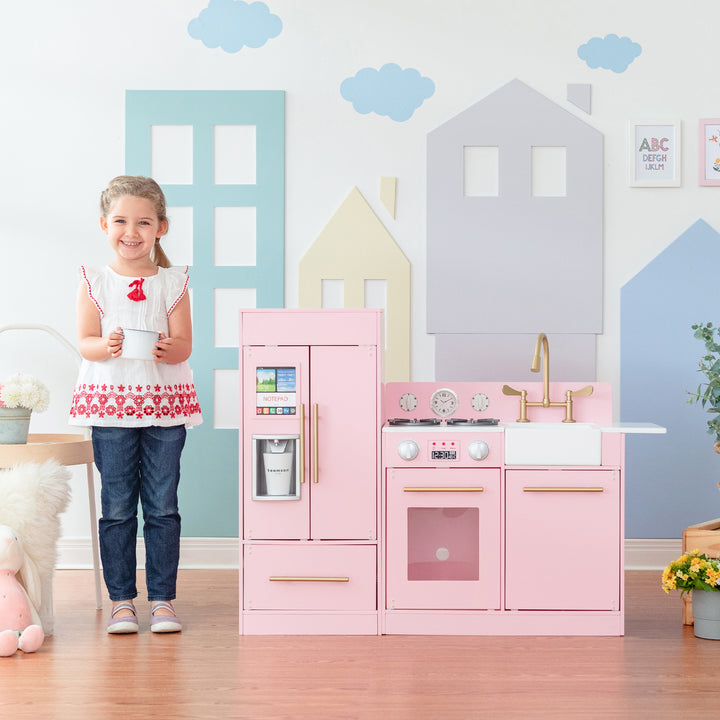 A little girl standing next to a modern pink play kitchen