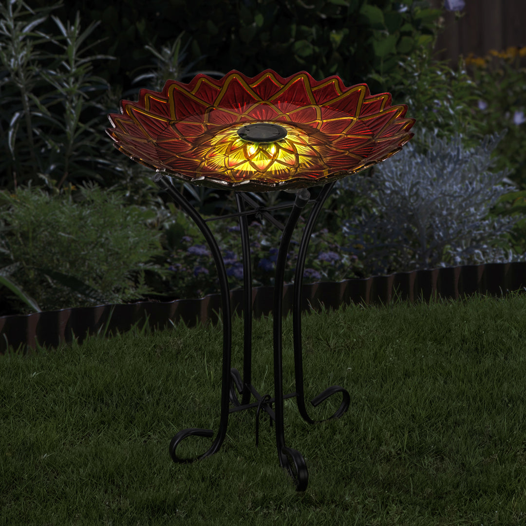 17.8" Dahlia Fusion Glass Birdbath with Solar-Powered Light, Red on a metal stand at night.