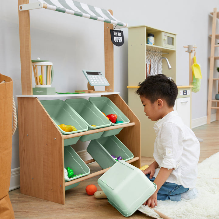 A little boy kneeling in front of the bins on a play market stand