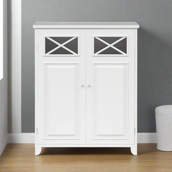 A white storage cabinet with two doors, featuring crossed detailing at the top, stands against a gray wall on a wooden floor. A small white basket is partially visible on the right.
