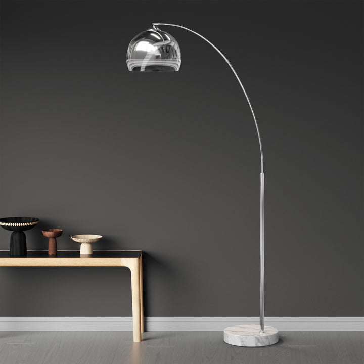 An arc lamp with a chrome lamp shade against a dark wall