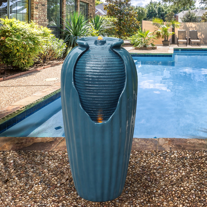 A tall blue faux vase water fountain next to a swimming pool
