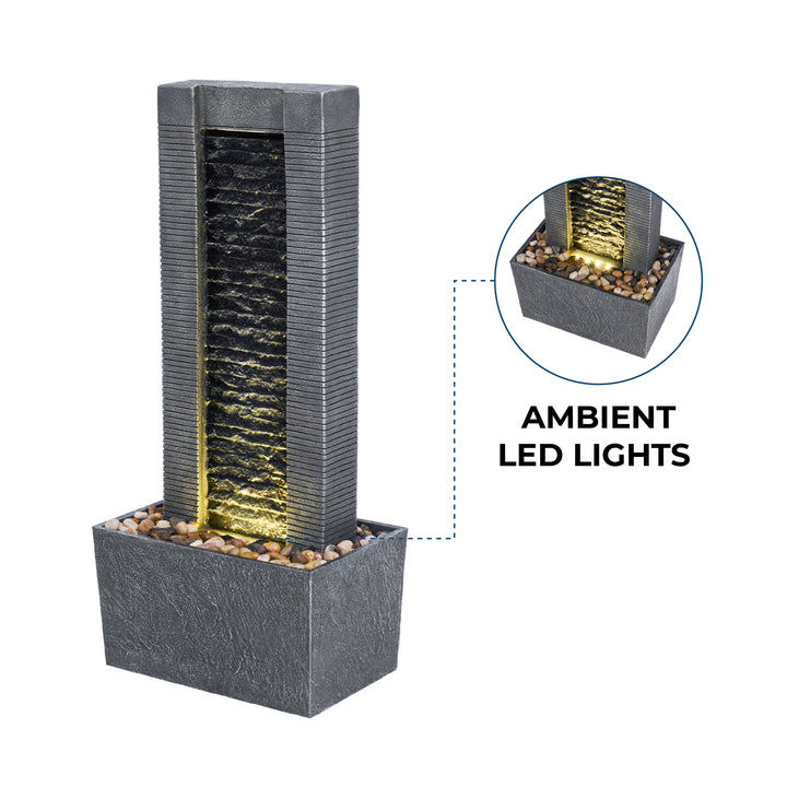 A tall, modern rectangular water fountain with ribbed texture and ambient LED lights, set on a rectangular base filled with small pebbles. Detailed view of the base with lights is shown in an inset.