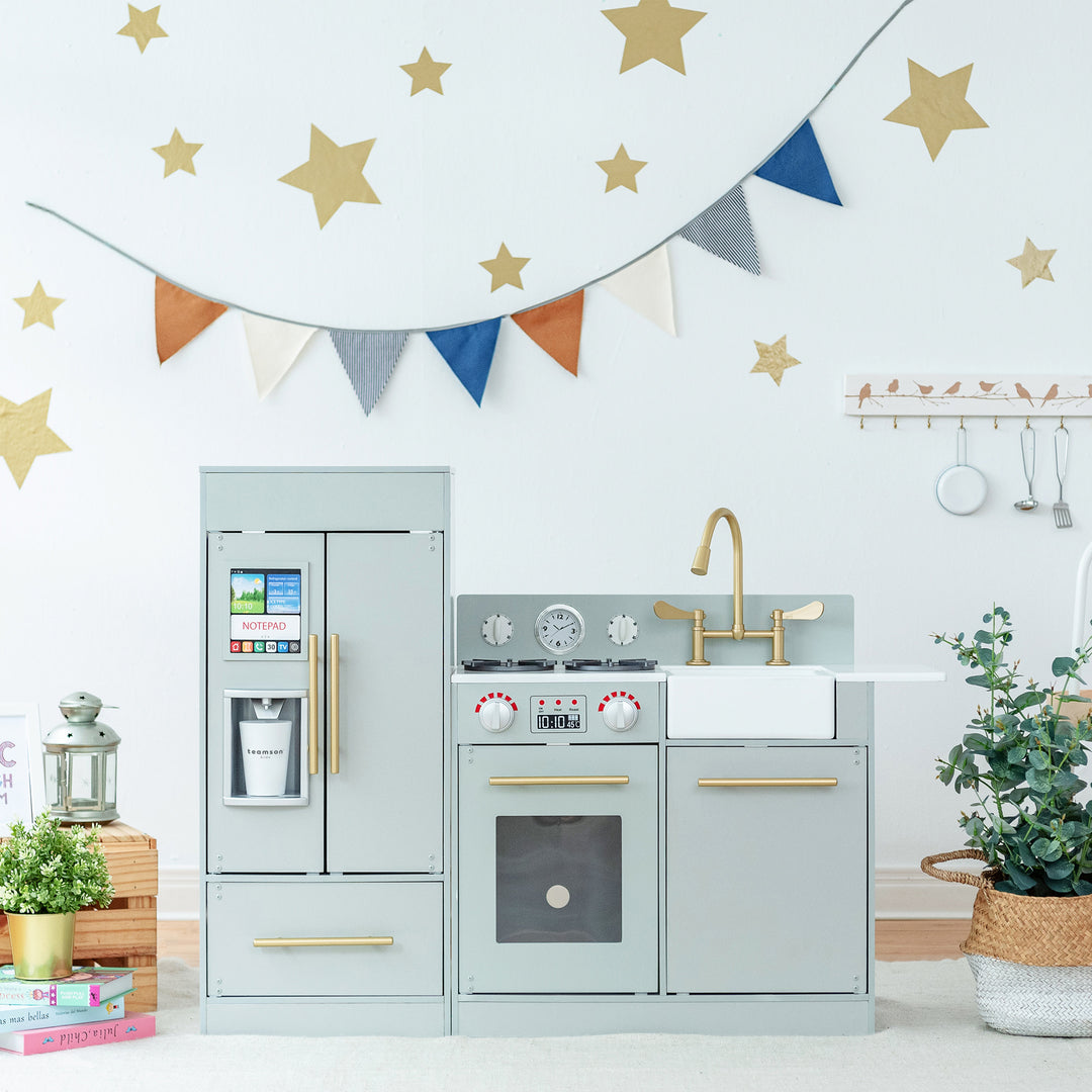 A child's Teamson Kids Little Chef Charlotte Modern Play Kitchen in a room decorated with star decals and a bunting garland.