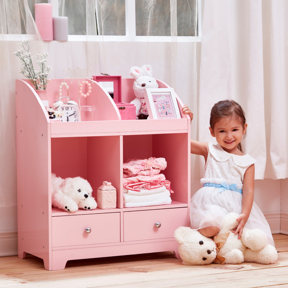 A little girl standing next to a Fantasy Fields Little Princess Cindy 3 Tier Toy Cubby Storage with Drawers, Pink with teddy bears.