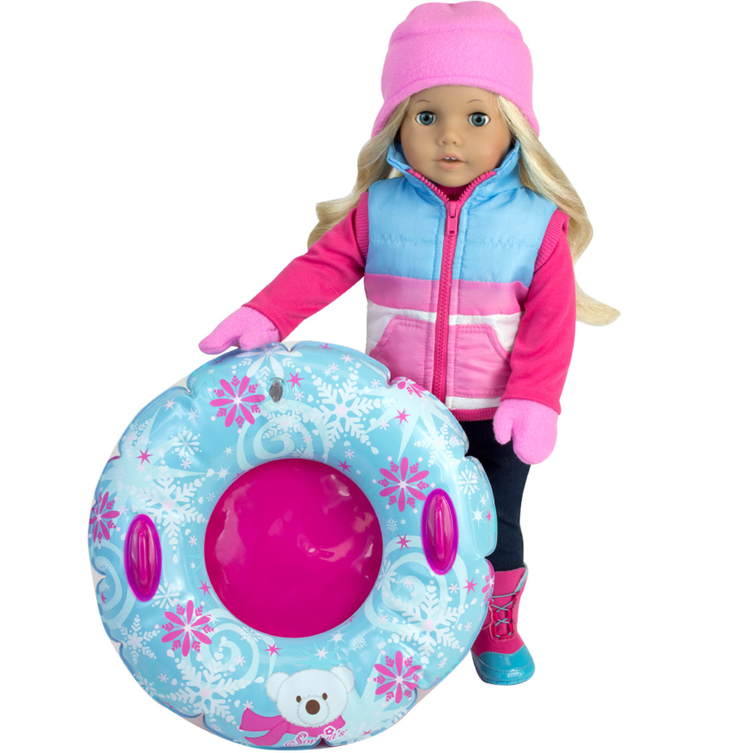 A blonde 18" doll with blue eyes dressed in a pink hat and gloves, blue and pink skivest blue and pink snow boots, and navy leggings holding a polar-themed snow innertube.