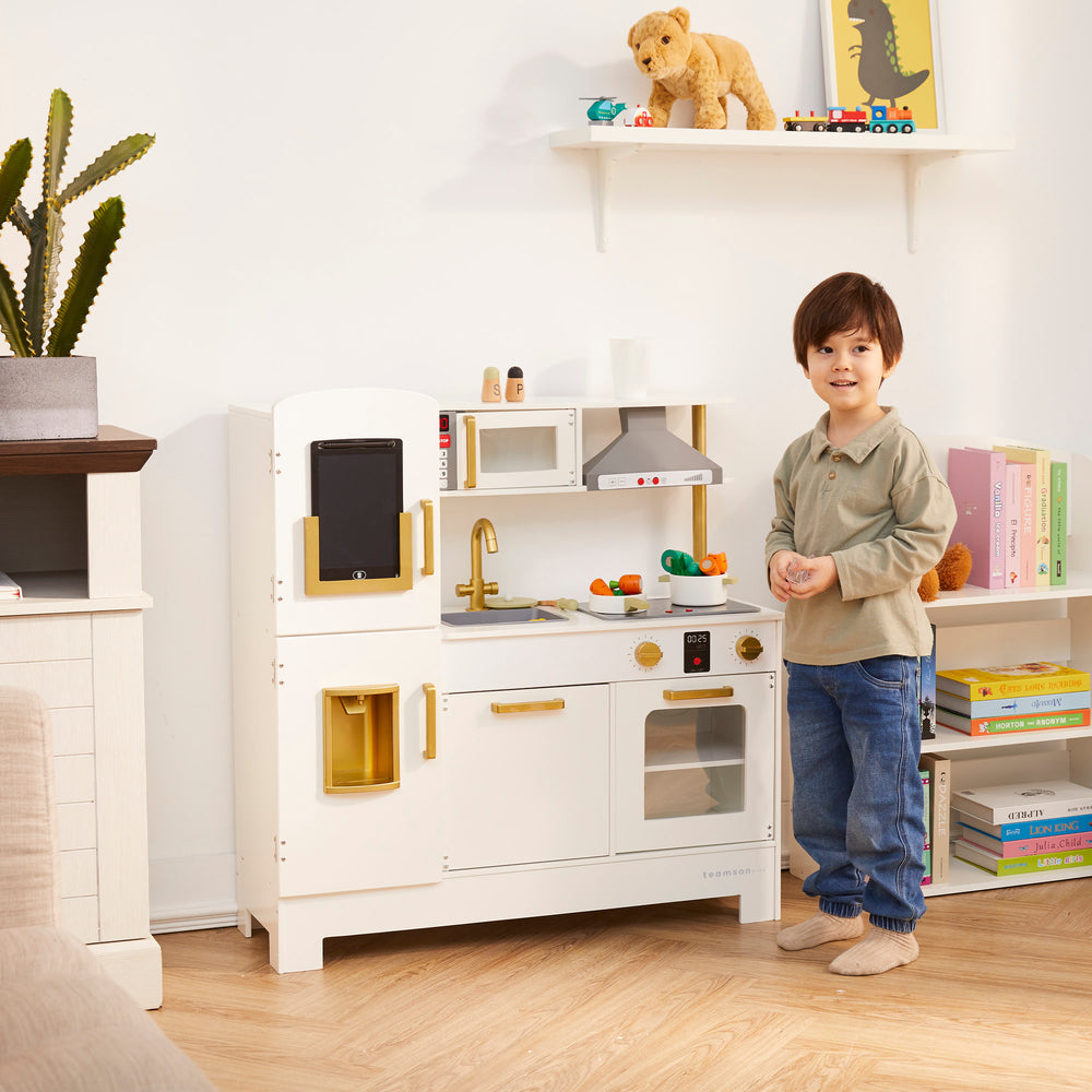 Child standing in a playroom next to the Teamson Kids All-in-One Little Chef Munich Play Kitchen.