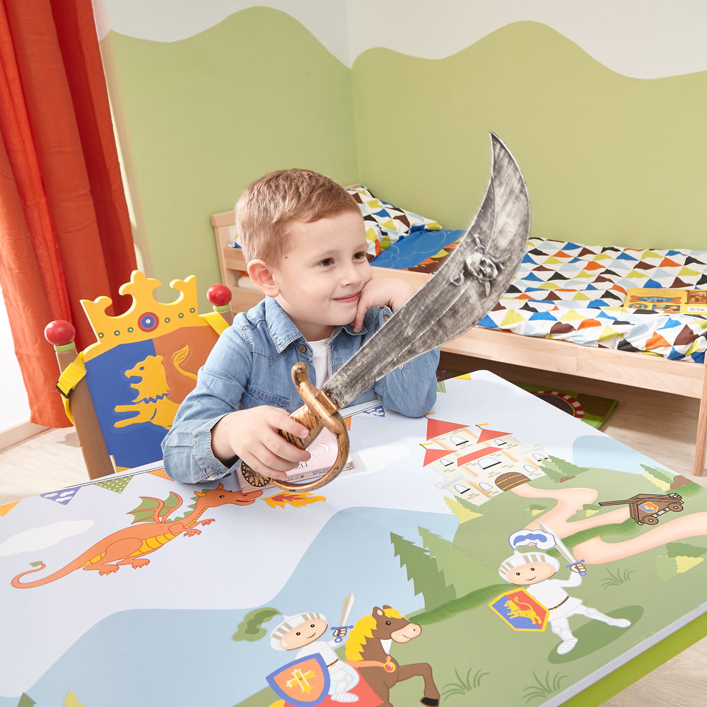 A young boy sitting at a table with a Fantasy Fields Kids Painted Wooden Knights and Dragons Table, Multicolor.