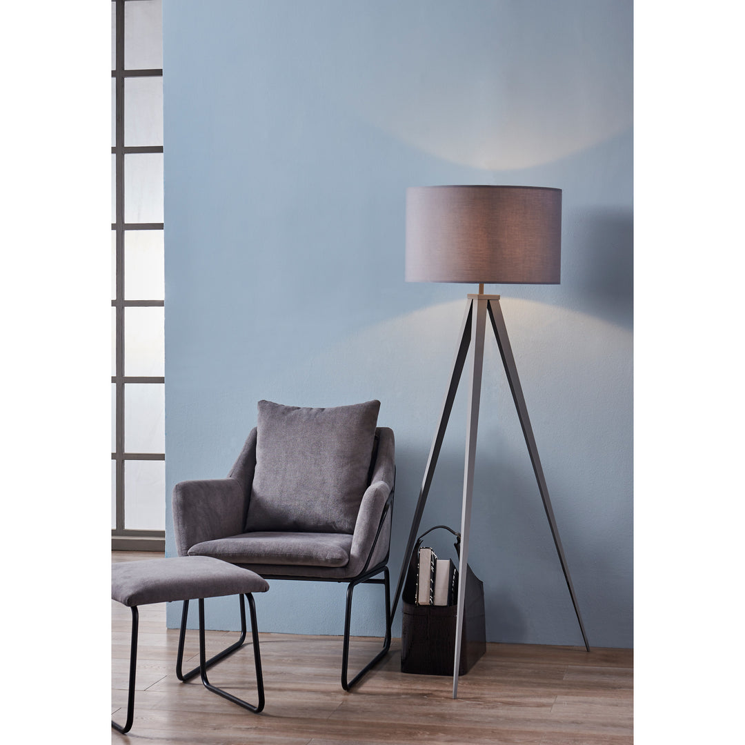 A modern reading nook with a stylish armchair, ottoman, Teamson Home Romanza 62" Postmodern Tripod Floor Lamp with Drum Shade, Gray, and books by a window with natural light.