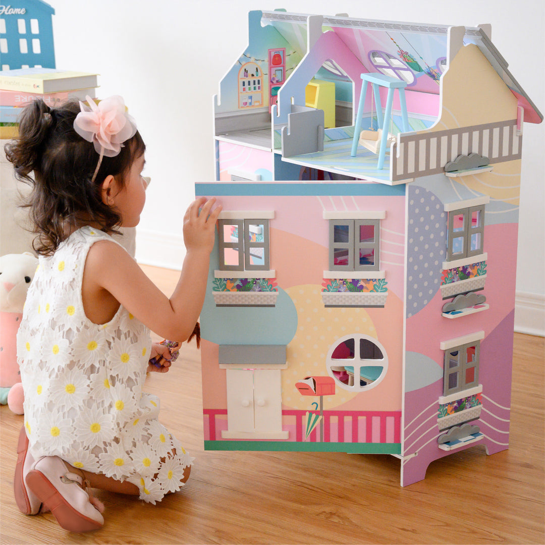 A little girl kneeling in front of a dollhouse with her doll in hand.