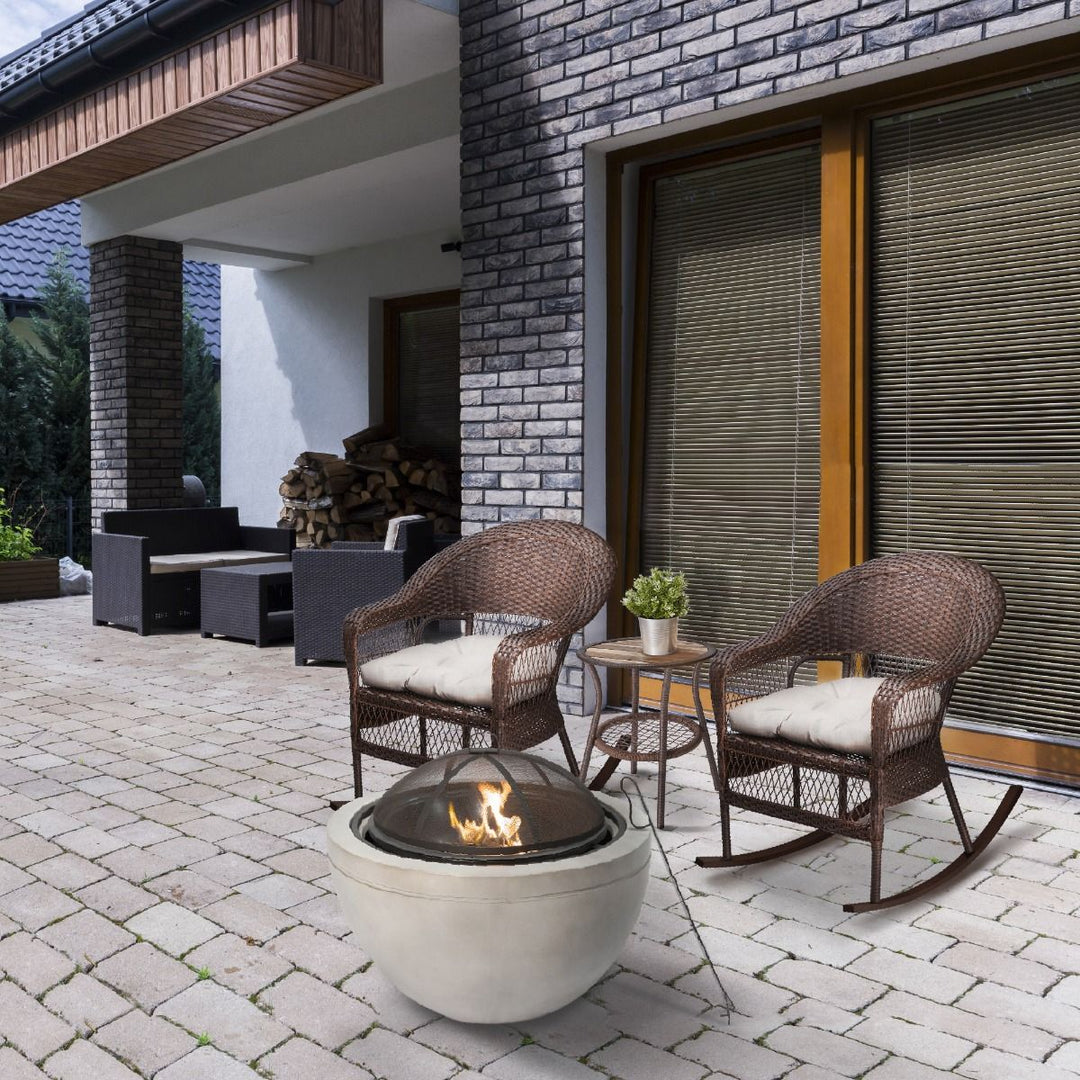 Two outdoor wicker patio rocking chairs sit in front of a round concrete Teamson fire pit.