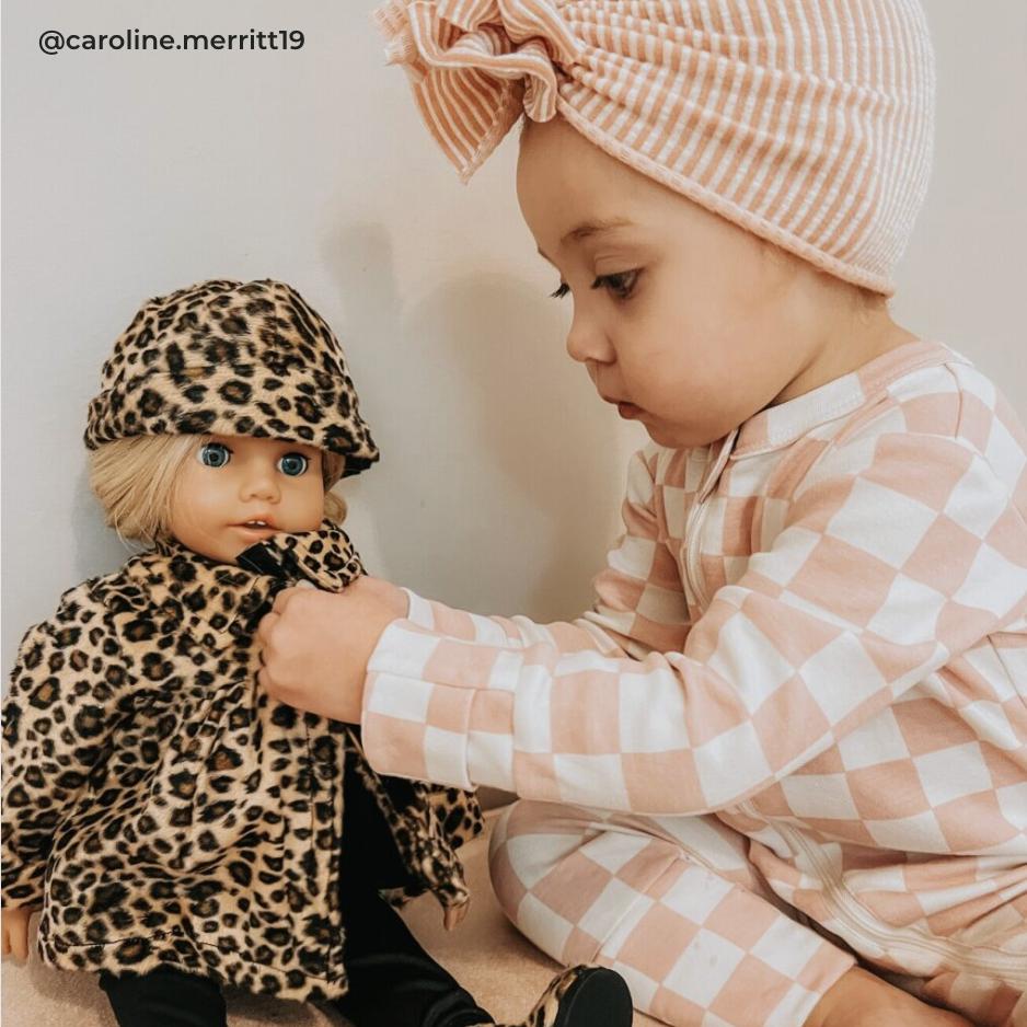 Young child dressing up her Sophia's doll in a leopard print jacket.