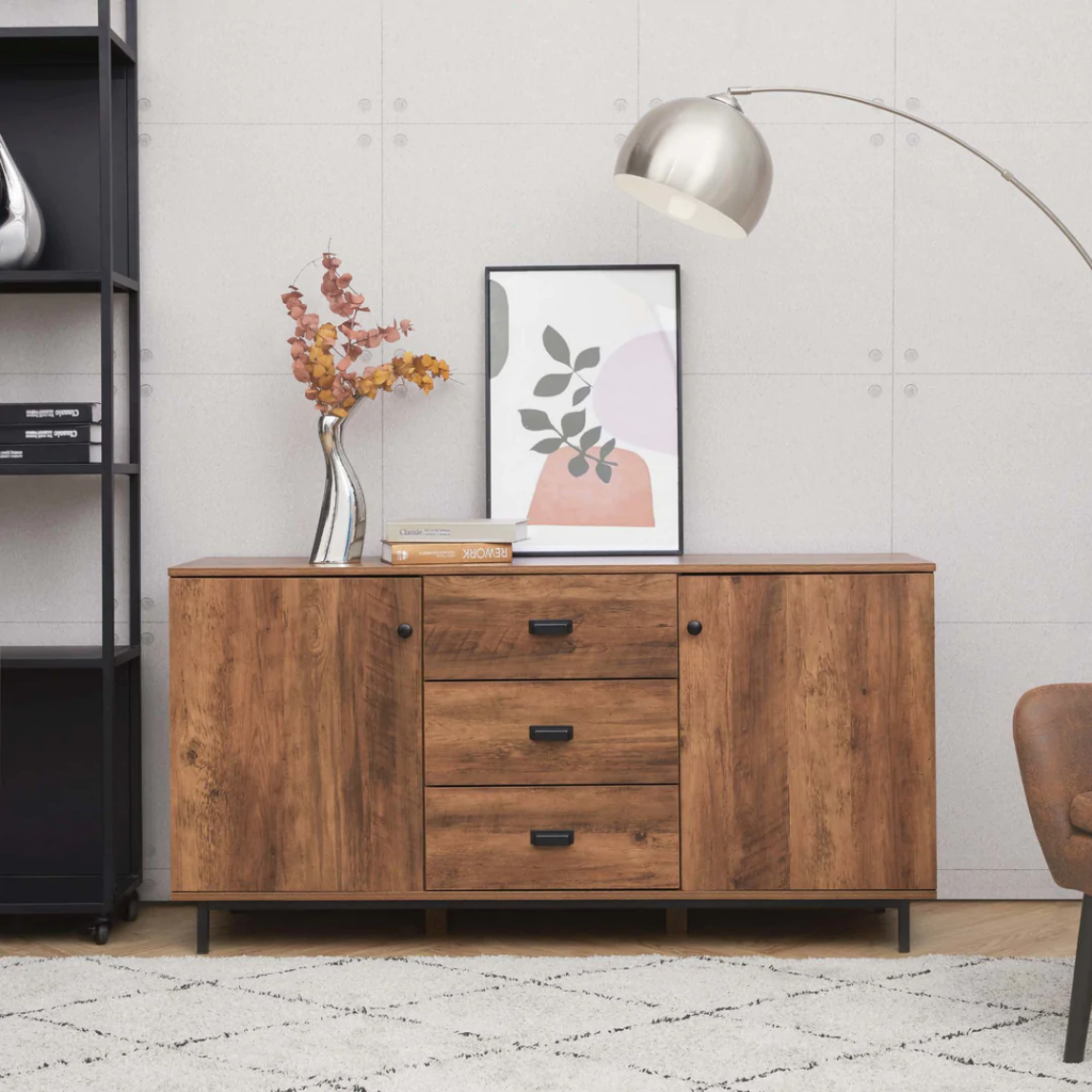 Light brown sideboard sits next to a white wall and features a flower painting resting above it.