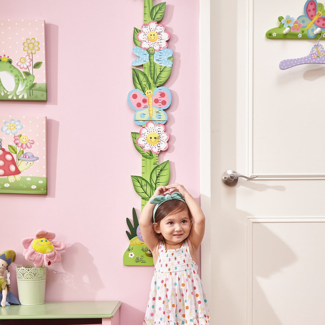 Little girl stand next to a height chart in her pink room.