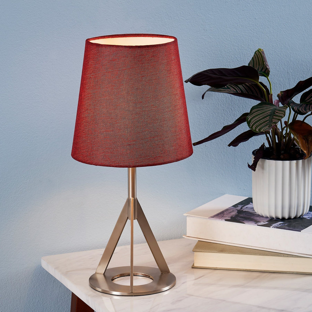A table lamp with a red shade and silver base sits on top of a faux white marble table top.