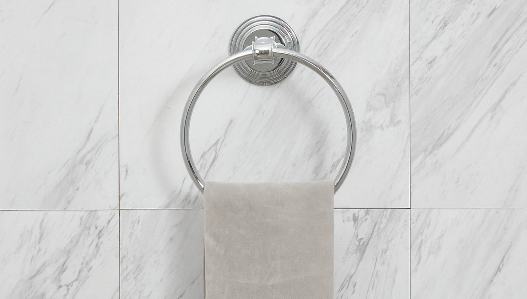 A chrome, round towel holder is shown on a marble tile bathroom wall.