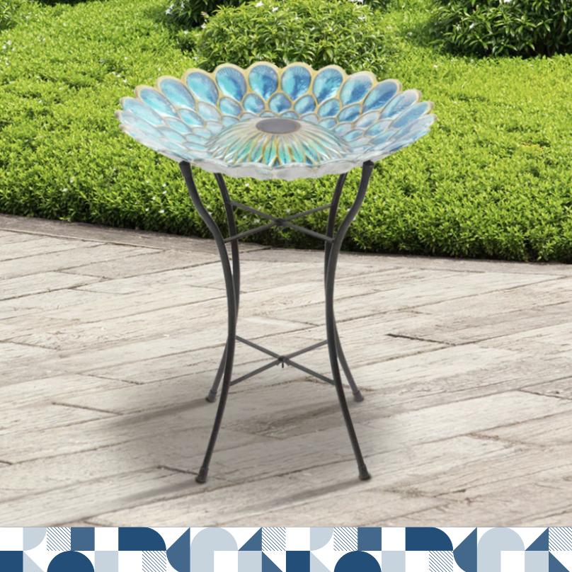 A glass bird bath with a solar light shaped like a flower with blue and green glass