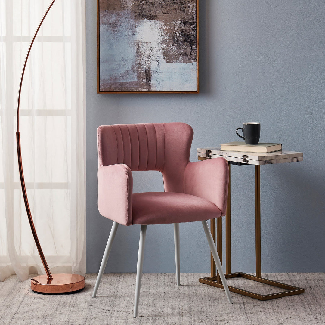 A modern pink accent chair sits next to a teamson faux marble side table holding a few books and a black coffee mug.
