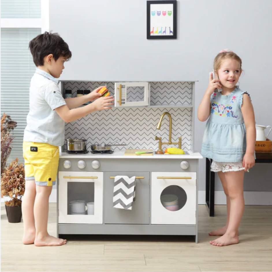 Two young kids play with a child sized kitchen