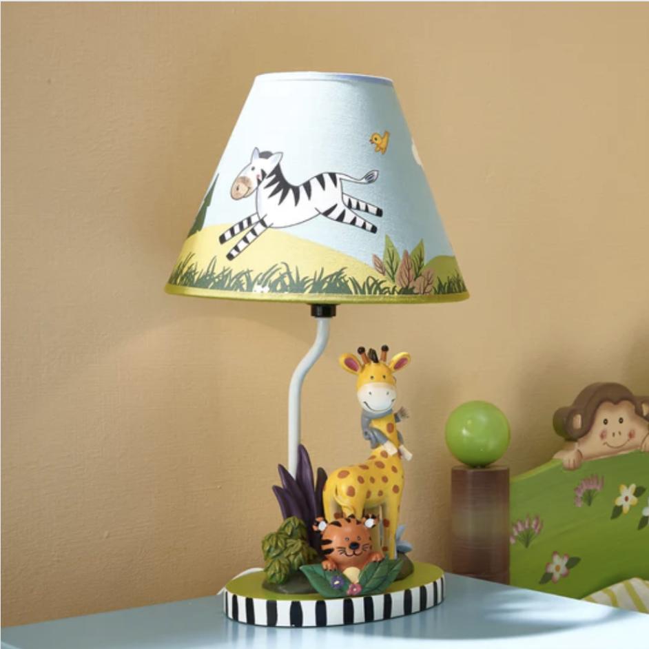 A table lamp with a giraffe and tiger on the base and a zebra on the shade sits next to a child's monkey-themed bed