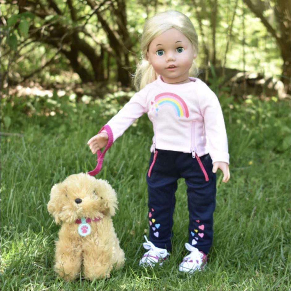 An 18 inch Sophia doll walks her pet doll-sized dog on a a leash outside.