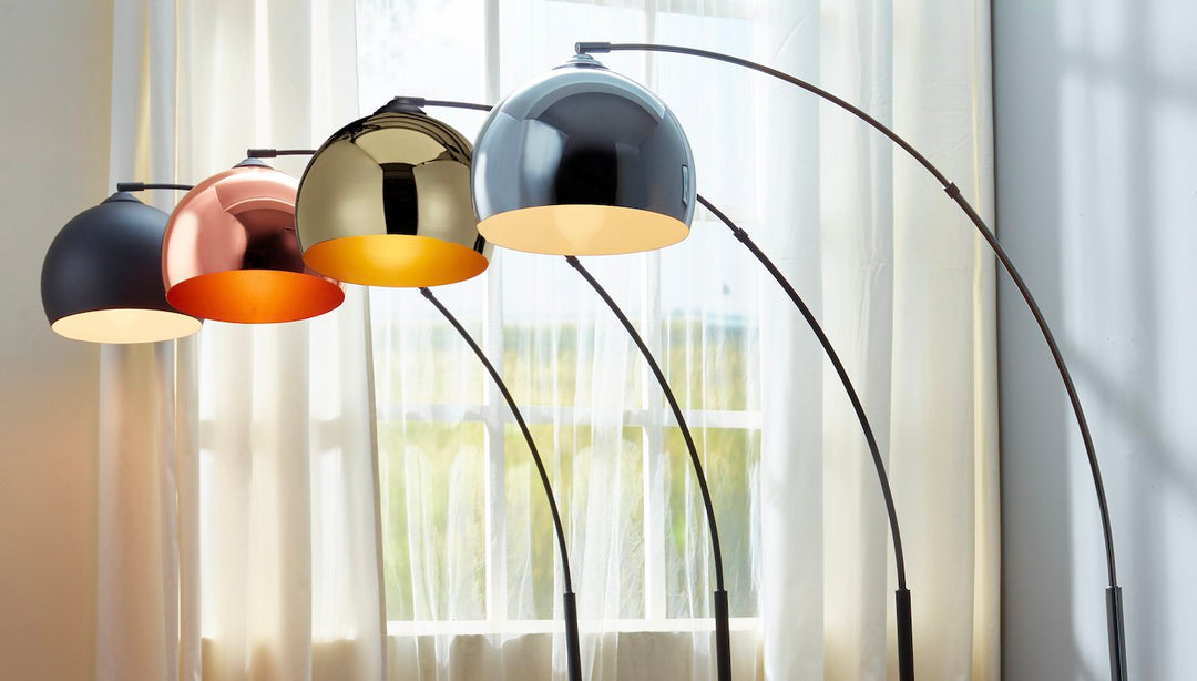 A row of arc lamps with alternating colored shades: black, rose gold, gold, and chrome.