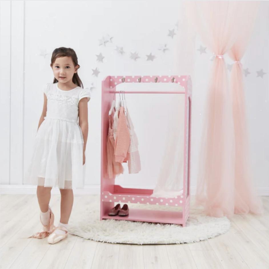 A little girl stands in front of her pink with white polka dot wardrobe.