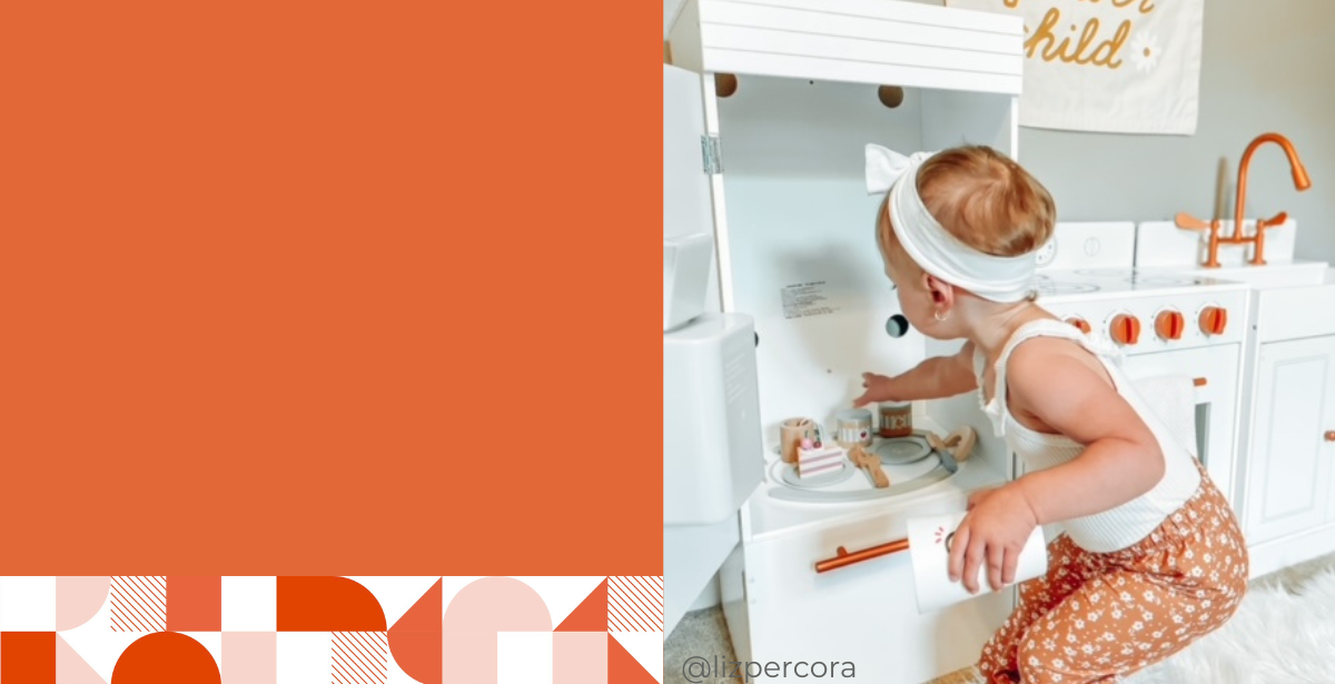 Toddler girl is playing with a white toy play kitchen. The play kitchen has the refrigerator door open showing a play cake set inside. The white kitchen has a gold faucet and handles. 
