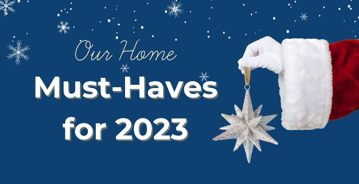 Our Home Must-Haves for 2023 is the text on a blue background with a santa hand holding an ornament