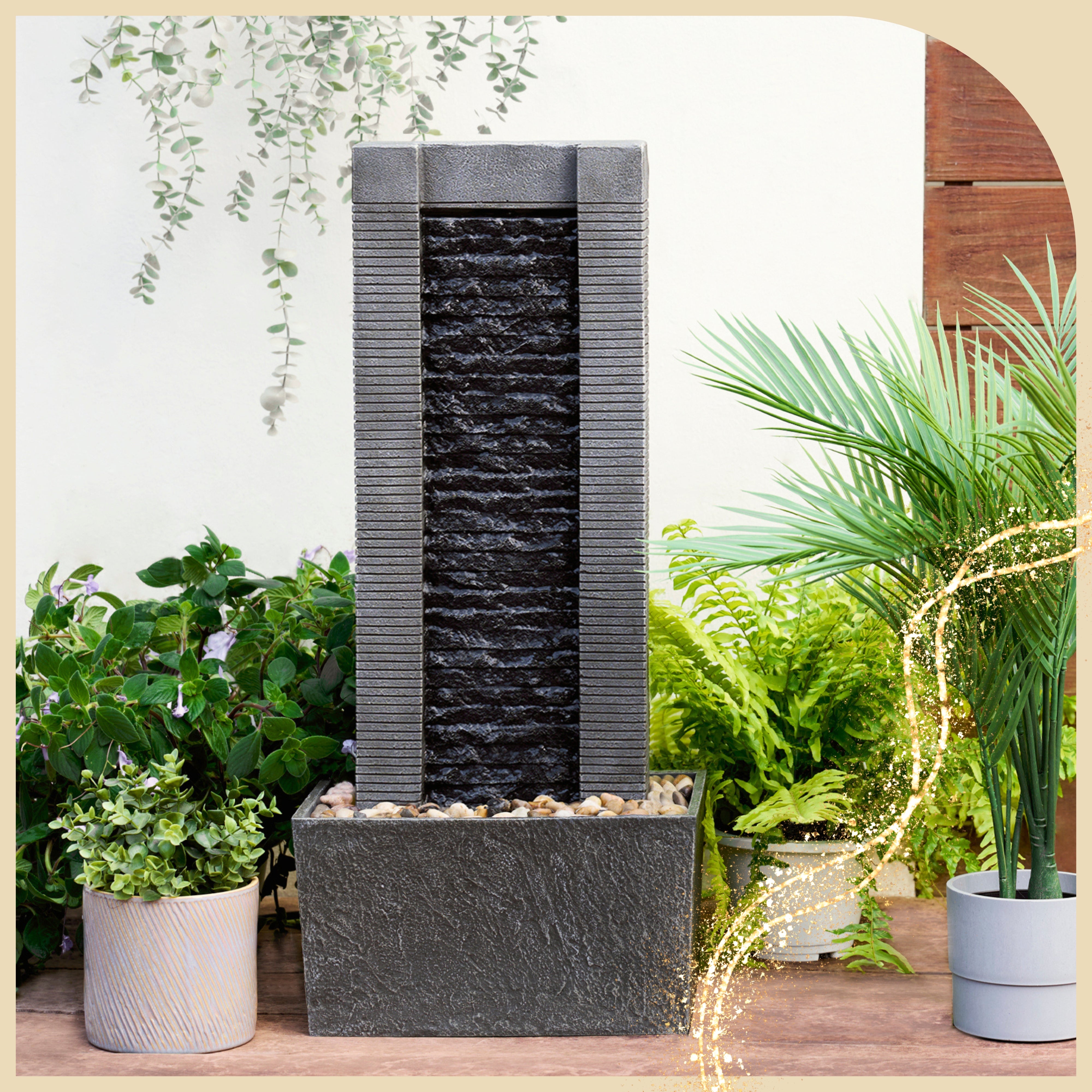 a sleek water fountain stands tall in an outdoor area with potted plants 