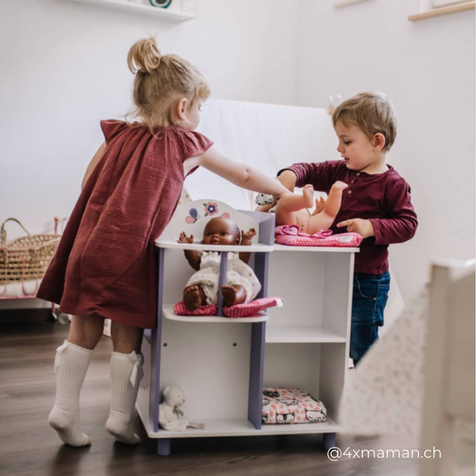 A little girl and little boy playing with two dolls - one doll in a highchair, one doll being dressed