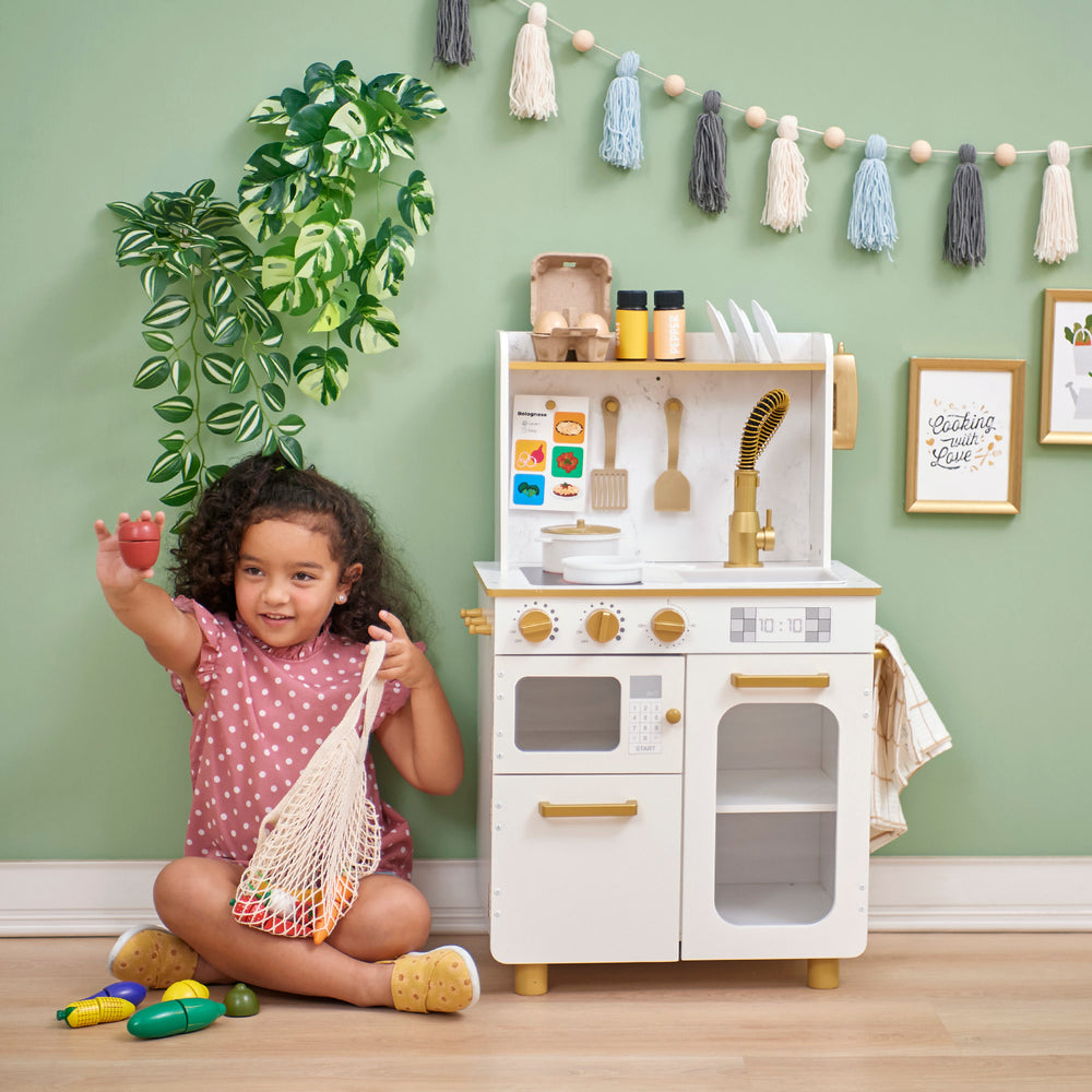 A young child playing with a Teamson Kids - Little Chef Memphis Small Play Kitchen set and accessories, smiling and raising one hand.