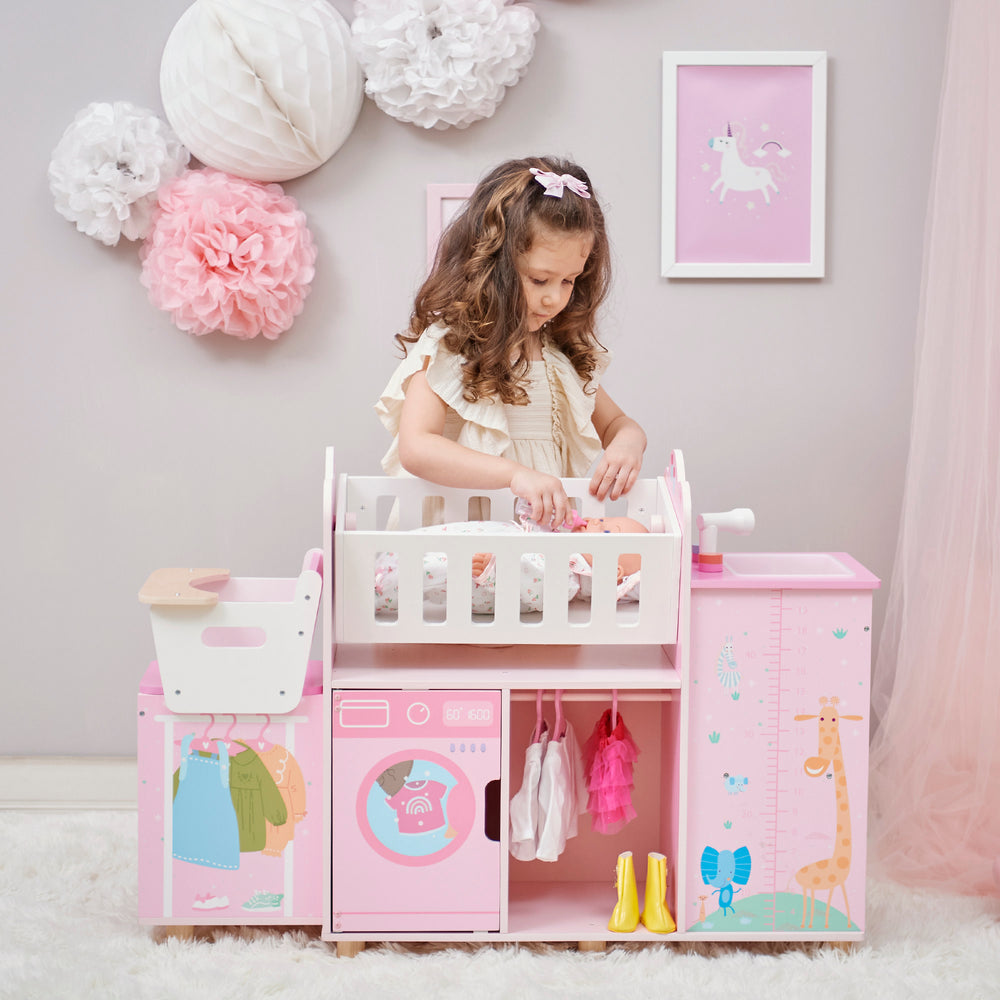 A girl feeding her baby doll laying in the cradle on the baby doll nursery station in pink with animal illustrations.