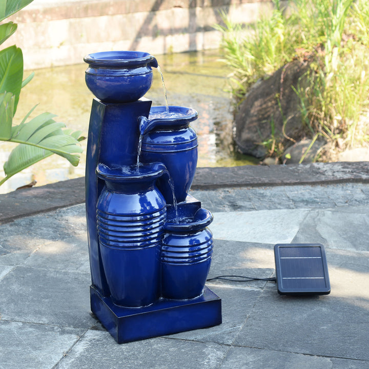 Teamson Home 28.74" Navy Blue 4-Tier Outdoor Solar Water Fountain with LED Lights off on a stone patio with the solar panel to the right