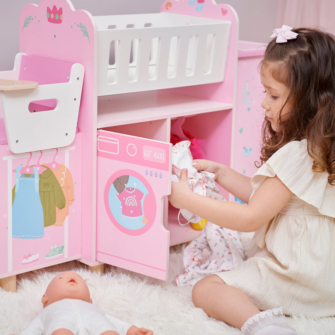 A little girl putting doll clothes in the pretend washing machine on the baby doll nursery station in pink with animal illustrations.
