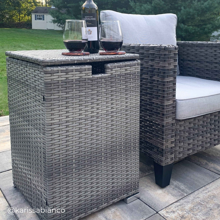 Grey outdoor storage box for propane tank in a backyard patio with wine glasses on top.