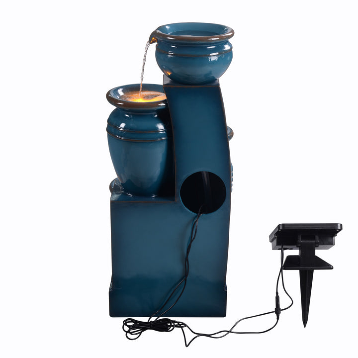 A back view of the Teamson Home 28.74" Blue 4-Tier Outdoor Solar Water Fountain with a cutout where the pump goes inside the fountain, and the cord connected to the solar panel