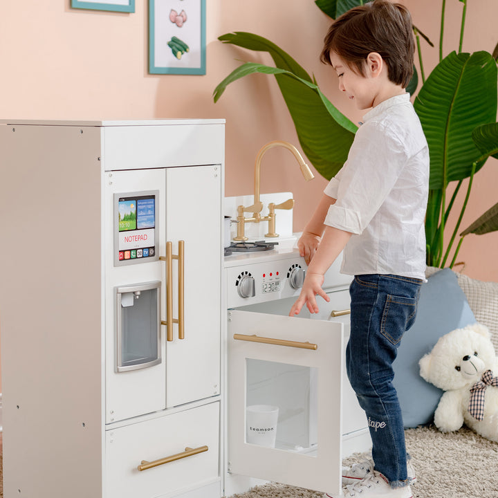 A child plays with a Teamson Kids Little Chef Charlotte Modern play kitchen set in a room with a pastel color scheme.
