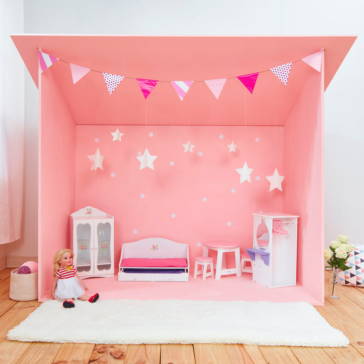 A room set up with pink walls and pink and white bunting with white furniture with floral accents: closet, trundle bed, table and two stools, and a wardrobe with a mirror.