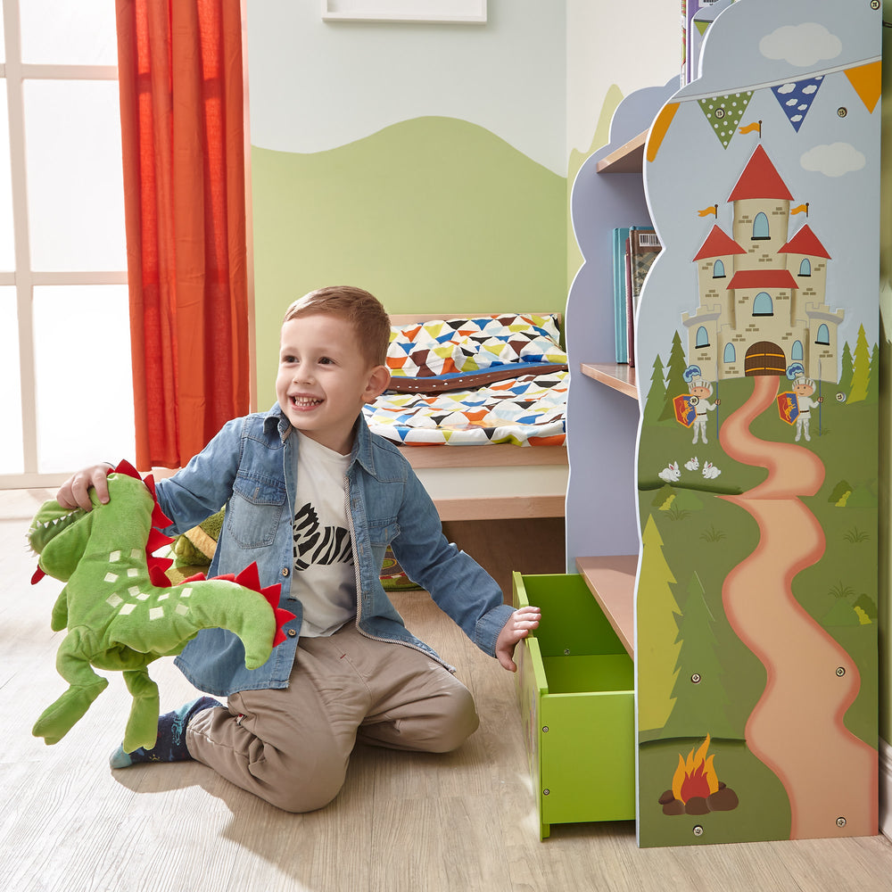 A young boy playing with a stuffed dragon closing the bottom drawer of the bookshelf in his bedroom.